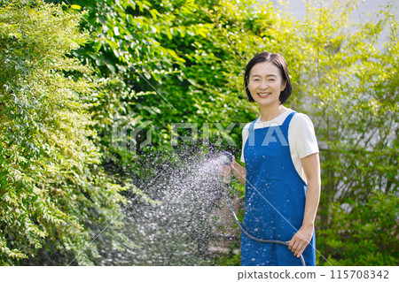 微笑的中年婦女在花園裡的綠樹澆水 115708342