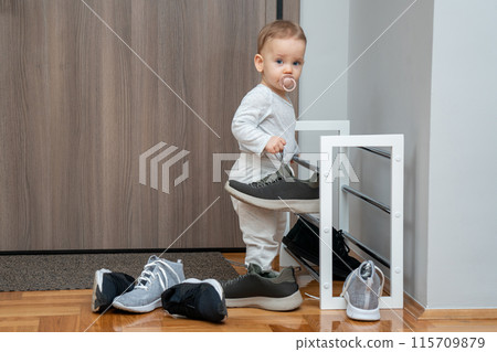 Toddler playing with adult dirty shoes in entryway. Concept of naughty baby having fun 115709879