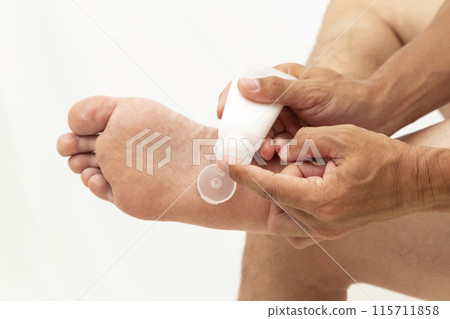 Man applying cream to the soles of his feet on a white background 115711858