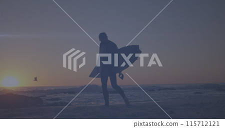 Spot of light moving against rear view of a man with surfboard walking at the beach 115712121