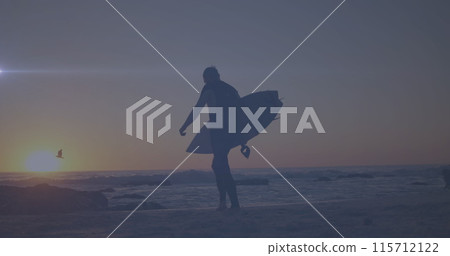 Spot of light moving against rear view of a man with surfboard walking at the beach 115712122