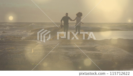 Glowing spots of light against african american couple holding hands running on the rocks 115712622