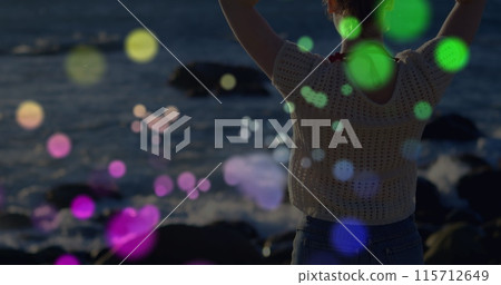 Colorful spots of light against rear view of caucasian woman standing on the rocks near the sea 115712649