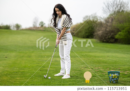 Beautiful woman striking the ball across the golf course 115713951