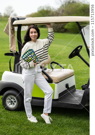 Sporty female player posing with the golf cart on the lawn 115713956