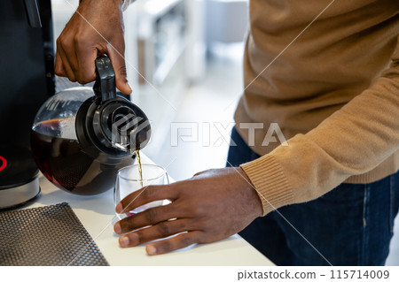 Anonymous man worker making a cup of hot coffee in the office kitchen 115714009