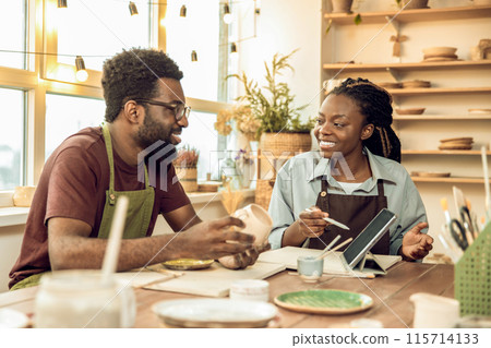 Man holding a clay mug in his hands and showing it to a woman Man holding a clay mug in his hands and showing it to a woman 115714133