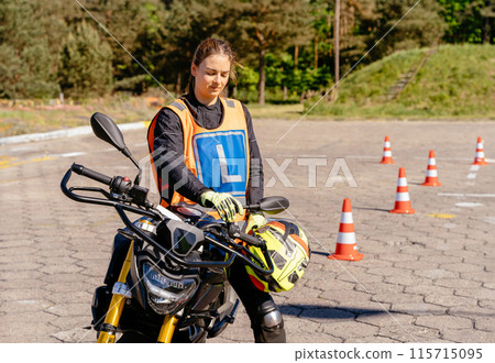 Moto school track driving school. Learning to ride motorcycle concept. Female L-driver relax after driving between cones, lesson in motorcycle school. Moto school track driving school. Learning to ride motorcycle concept. Female L-driver relax after driving between cones, lesson in motorcycle school. 115715095