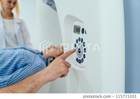 A man is pointing at a machine with a woman lying on it. The woman is wearing a white shirt and blue stripes. Mature patient in medical x-ray scanner 115715201
