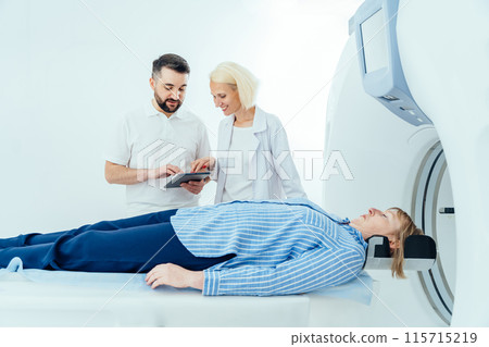 Male radiologist holding tablet, consulting with female doctor, patient lying on scanner bed during diagnostics. Computed tomography examination. Doctor consulting talk support to patient in hospital. 115715219