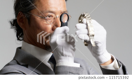 A male appraiser checking a watch with a magnifying glass A male appraiser checking a watch with a magnifying glass 115715392
