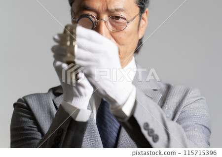 A male appraiser checking a watch with a magnifying glass A male appraiser checking a watch with a magnifying glass 115715396