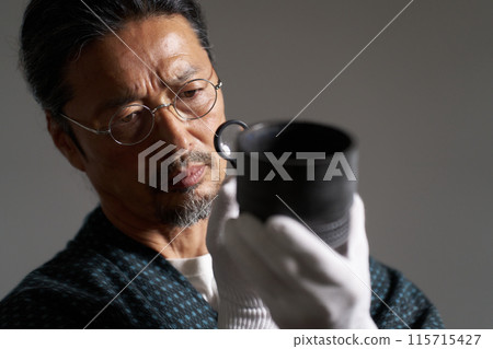 一位身穿日本服裝的男性鑑賞家用放大鏡檢查陶瓷的圖像 一位身穿日本服裝的男性鑑賞家用放大鏡檢查陶瓷的圖像 115715427