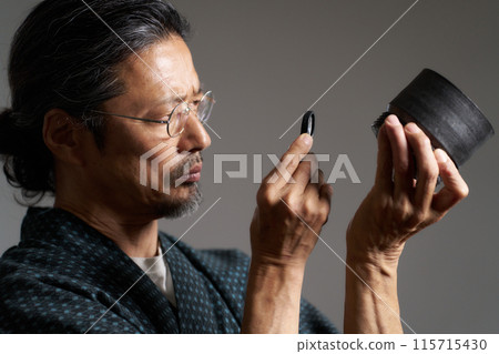 Image of a man in a kimono inspecting ceramics with a magnifying glass Image of a man in a kimono inspecting ceramics with a magnifying glass 115715430