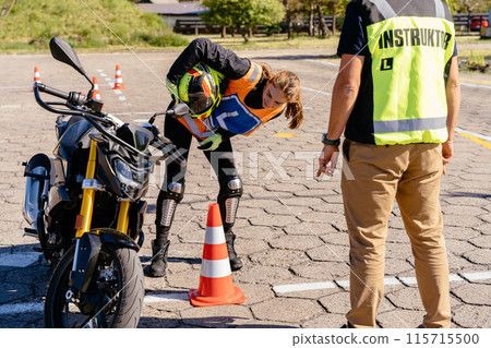 Learner biker on test road with red cones. Instructor writing on clipboard his points. Student and instructor, exam in motorcycle school. Learner biker on test road with red cones. Instructor writing on clipboard his points. Student and instructor, exam in motorcycle school. 115715500