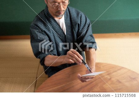 一個穿著日式服裝的男人在紙條上寫字 115715508