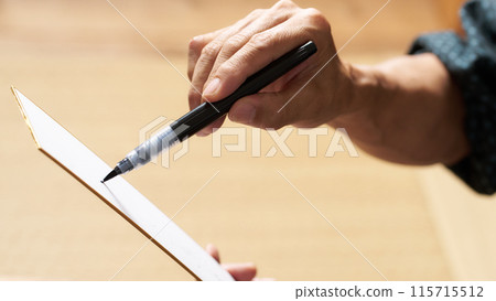A man's hand writing on a strip of paper with a brush pen A man's hand writing on a strip of paper with a brush pen 115715512