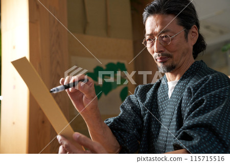 A man in kimono writing on a strip of paper 115715516