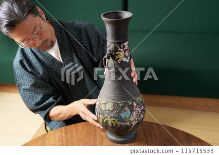 一個穿著日式服裝的男人拿起並檢查銅花瓶、鑑定師、古物學家、收藏家的形象 一個穿著日式服裝的男人拿起並檢查銅花瓶、鑑定師、古物學家、收藏家的形象 115715533