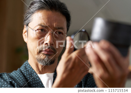 Image of a man in a kimono inspecting ceramics with a magnifying glass Image of a man in a kimono inspecting ceramics with a magnifying glass 115715534