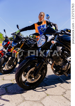 A woman wearing an orange vest is standing beside a line of motorcycles on display. The keywords include wheel, tire, sky, vehicle, motorcycle, and fuel tank 115715763