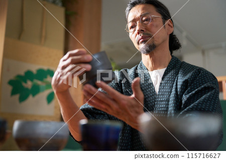 Image of a man in a kimono gazing at ceramics, a potter, an appraiser Image of a man in a kimono gazing at ceramics, a potter, an appraiser 115716627