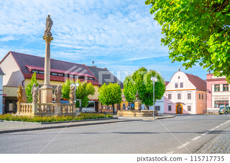 The Plague Column and Fountain in the town square of Pecka, Czechia. The column stands tall in the center, adorned with statues, while the fountain flows in the foreground. The Plague Column and Fountain in the town square of Pecka, Czechia. The column stands tall in the center, adorned with statues, while the fountain flows in the foreground. 115717735
