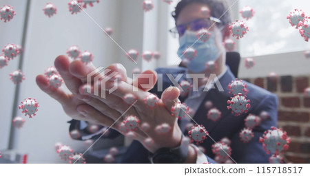 Image of covid 19 cells floating over man wearing face mask, sanitizing his hands in office 115718517