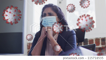 Image of covid 19 cells floating over worried biracial woman wearing face mask in office 115718535
