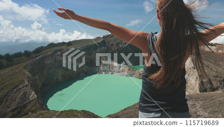 Tourist woman rises hands on volcanic Kelimutu blue crater lakes. Travel destination. Beautiful wild nature landscape. Exotic summer vacation, hiking, relax. Close up back view 4K zoom in Tourist woman rises hands on volcanic Kelimutu blue crater lakes. Travel destination. Beautiful wild nature landscape. Exotic summer vacation, hiking, relax. Close up back view 4K zoom in 115719689
