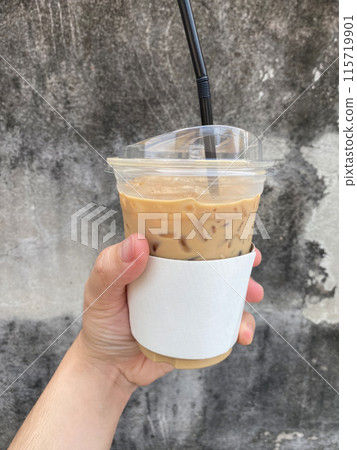 A hand holding a glass of iced milk tea against an old wall. 115719901