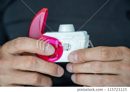 Close up view of man using medicine dry powder inhaler for treatment asthma or COPD diseases. Pharmaceutical product is used to treat lung inflammation and prevent asthma attack. Close up view of man using medicine dry powder inhaler for treatment asthma or COPD diseases. Pharmaceutical product is used to treat lung inflammation and prevent asthma attack. 115723125