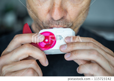 Close up view of man using medicine dry powder inhaler for treatment asthma or COPD diseases. Pharmaceutical product is used to treat lung inflammation and prevent asthma attack. 115723142