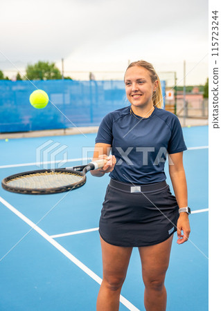 Professional female tennis player posing with the tennis racket and ball on outside court Professional female tennis player posing with the tennis racket and ball on outside court 115723244