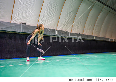 Sports young woman with racket and shuttlecock is exercising, playing in badminton on inside court Sports young woman with racket and shuttlecock is exercising, playing in badminton on inside court 115723328