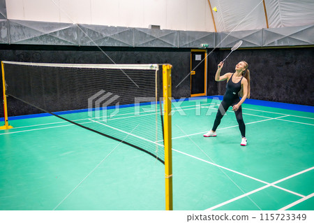 Sports young woman with racket and shuttlecock is exercising, playing in badminton on inside court Sports young woman with racket and shuttlecock is exercising, playing in badminton on inside court 115723349