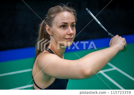 Sports young woman with racket and shuttlecock is posing before playing in badminton on inside court Sports young woman with racket and shuttlecock is posing before playing in badminton on inside court 115723359