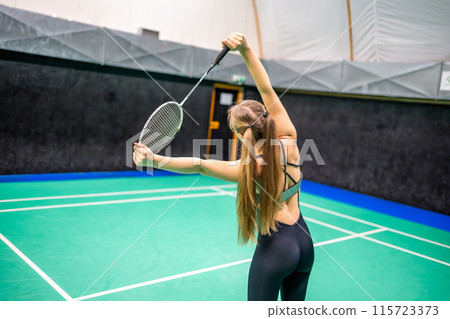 Sports young woman with racket and shuttlecock is exercising, doing warm-up before playing in badminton on inside court 115723373
