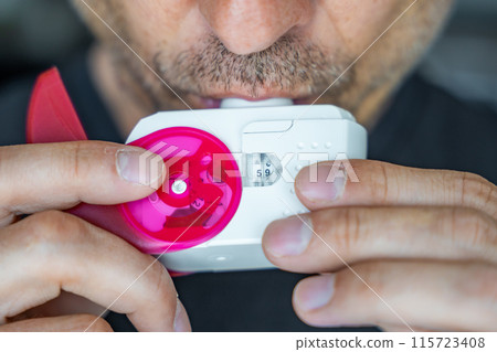 Close up view of man using medicine dry powder inhaler for treatment asthma or COPD diseases. Pharmaceutical product is used to treat lung inflammation and prevent asthma attack. 115723408