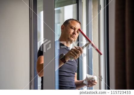 Young man cleans the windows in the house. He splashes detergent, rubs and removes water at the glass 115723433
