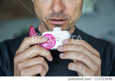 Close up view of man using medicine dry powder inhaler for treatment asthma or COPD diseases. Pharmaceutical product is used to treat lung inflammation and prevent asthma attack. 115723640