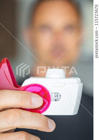Close up view of man using medicine dry powder inhaler for treatment asthma or COPD diseases. Pharmaceutical product is used to treat lung inflammation and prevent asthma attack. Close up view of man using medicine dry powder inhaler for treatment asthma or COPD diseases. Pharmaceutical product is used to treat lung inflammation and prevent asthma attack. 115723678