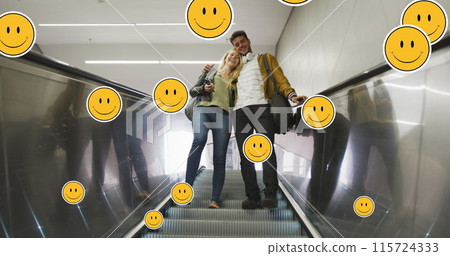 Image of digital emoji icons floating over happy caucasian couple embracing on moving stairs 115724333