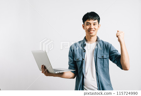 Portrait smiling Asian young man hold a laptop computer studio shot isolated white background, happiness and excited man holding laptop and raising his arm up to celebrate success Portrait smiling Asian young man hold a laptop computer studio shot isolated white background, happiness and excited man holding laptop and raising his arm up to celebrate success 115724990