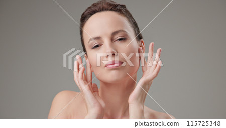 Beauty, health, cosmetics, anti-aging therapy and skin care concept - young beautiful brunette Caucasian woman touching face and looking at camera Beauty, health, cosmetics, anti-aging therapy and skin care concept - young beautiful brunette Caucasian woman touching face and looking at camera 115725348