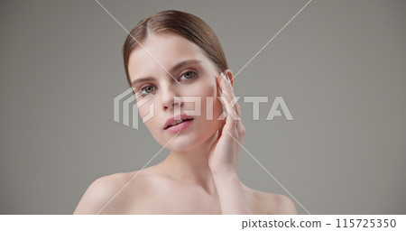 Beauty, health, cosmetics, anti-aging therapy and skin care concept - young beautiful brunette Caucasian woman posing and looking at the camera with a calm confident look like in a mirror Beauty, health, cosmetics, anti-aging therapy and skin care concept - young beautiful brunette Caucasian woman posing and looking at the camera with a calm confident look like in a mirror 115725350