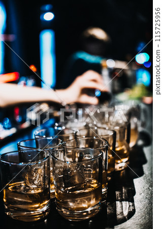 Bartender Preparing Multiple Whiskey Cocktails at a Busy Bar 115725956