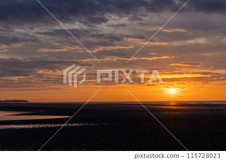 Enjoy a stunning coastal sunset with dramatic clouds and reflections in a serene landscape 115728023