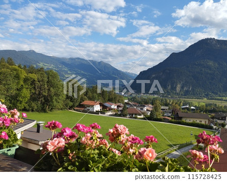 Idyllic view from balcony with geranium flowers in the village of Wiesing towards green valley with Alps and Lake Achensee in Tyrol, Austria. Summer sunny day. Idyllic view from balcony with geranium flowers in the village of Wiesing towards green valley with Alps and Lake Achensee in Tyrol, Austria. Summer sunny day. 115728425
