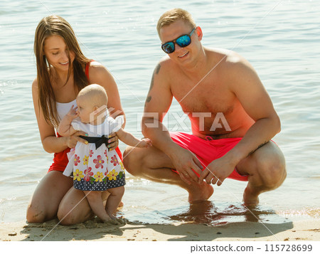 Two adult and baby posing near water 115728699